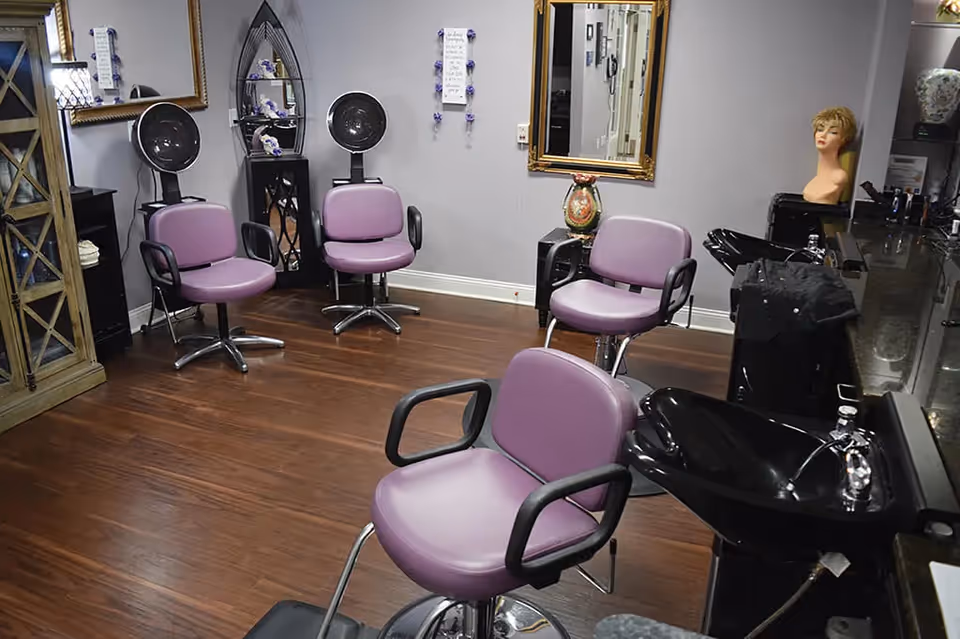 Interior salon with purple styling chairs, hooded dryers, hair-wash sinks, and a mannequin head.