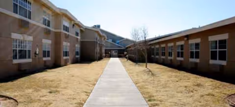 Long concrete walkway flanked by beige senior living buildings under a clear, sunny sky.