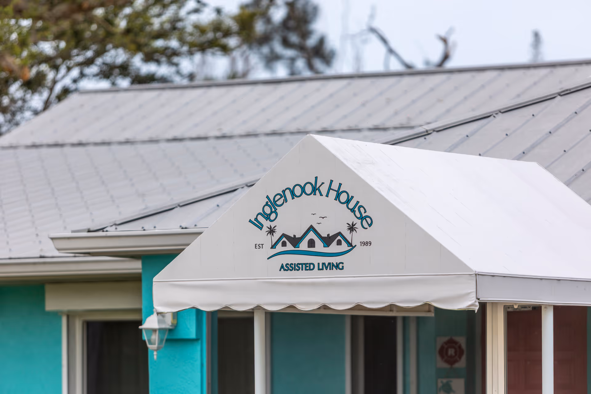 White entrance awning displaying the 'Inglenook House Assisted Living' logo over a teal building facade.