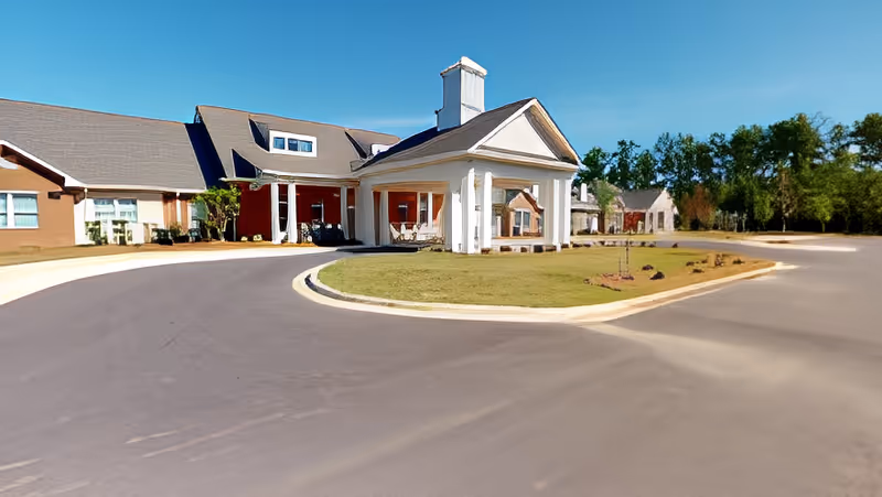 Front entrance and covered porte-cochere of a senior living facility with a curved driveway and landscaped center island.