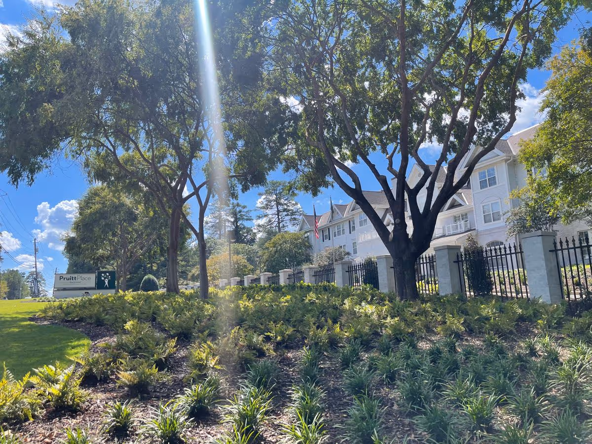 Exterior front of PruittPlace - Buckhead senior living building behind trees, a fence, and landscaped grounds.