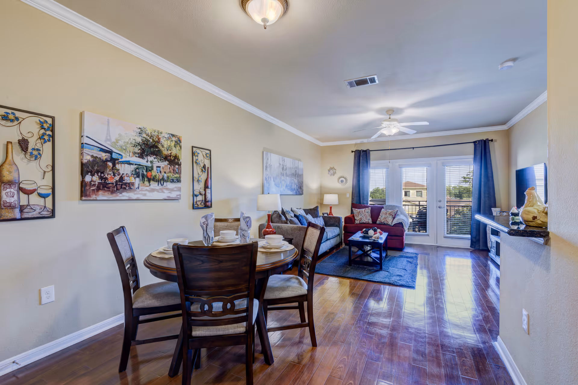 Open-concept living and dining area with a round dining table in the foreground, couches and a coffee table facing glass doors to a balcony.