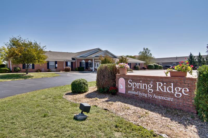 Front exterior and entrance of the Spring Ridge assisted living building with a brick sign and landscaped grounds.