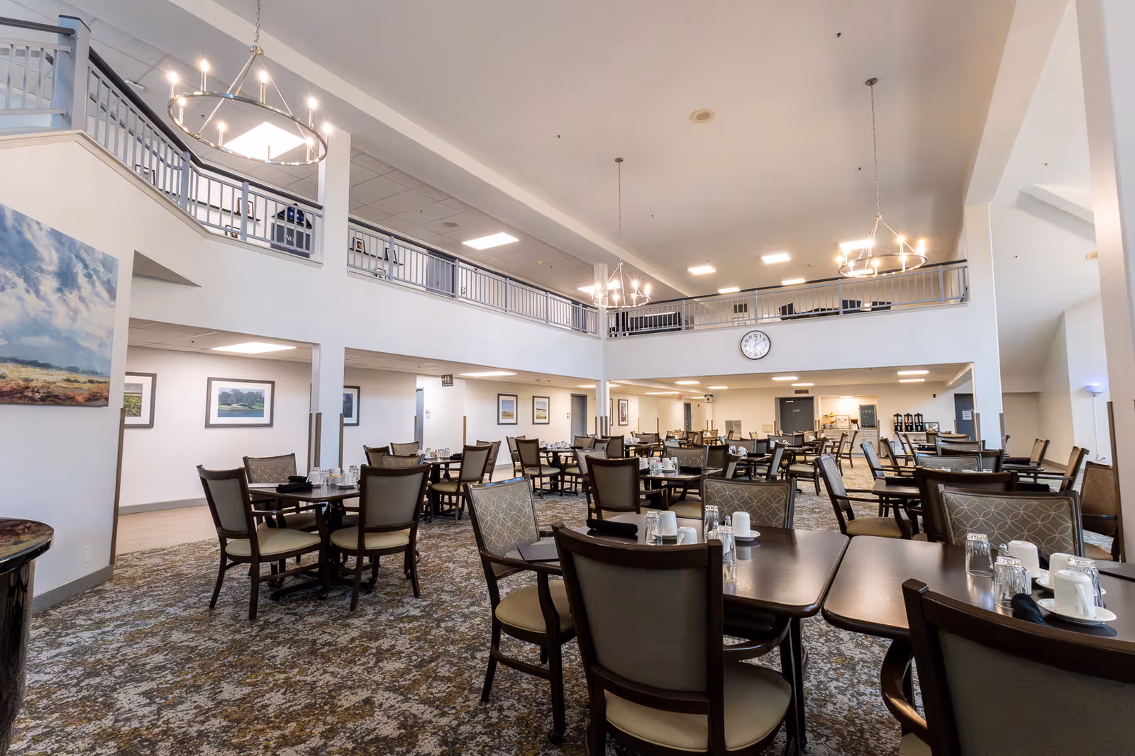 Large two-story dining room with multiple set tables, chandeliers, and a balcony overlooking the seating area.