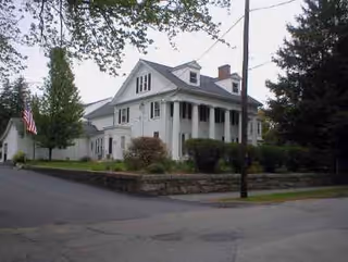Front view of Whitinsville Retirement Society facility with porch, flag, and landscaping