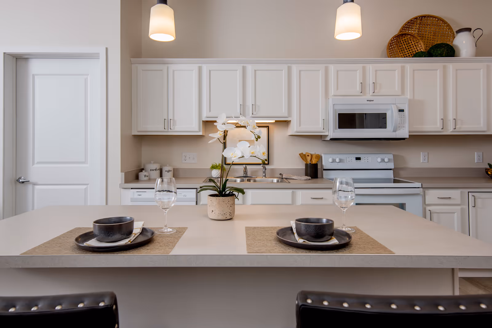 Bright modern kitchen with a center island set for two, white cabinets, microwave, and pendant lights.