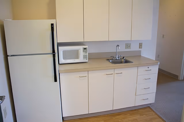 Small kitchenette with white cabinets, a countertop microwave, sink, and a refrigerator.
