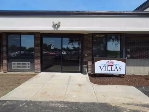 Front entrance of a senior living facility with glass doors and a Villas sign.