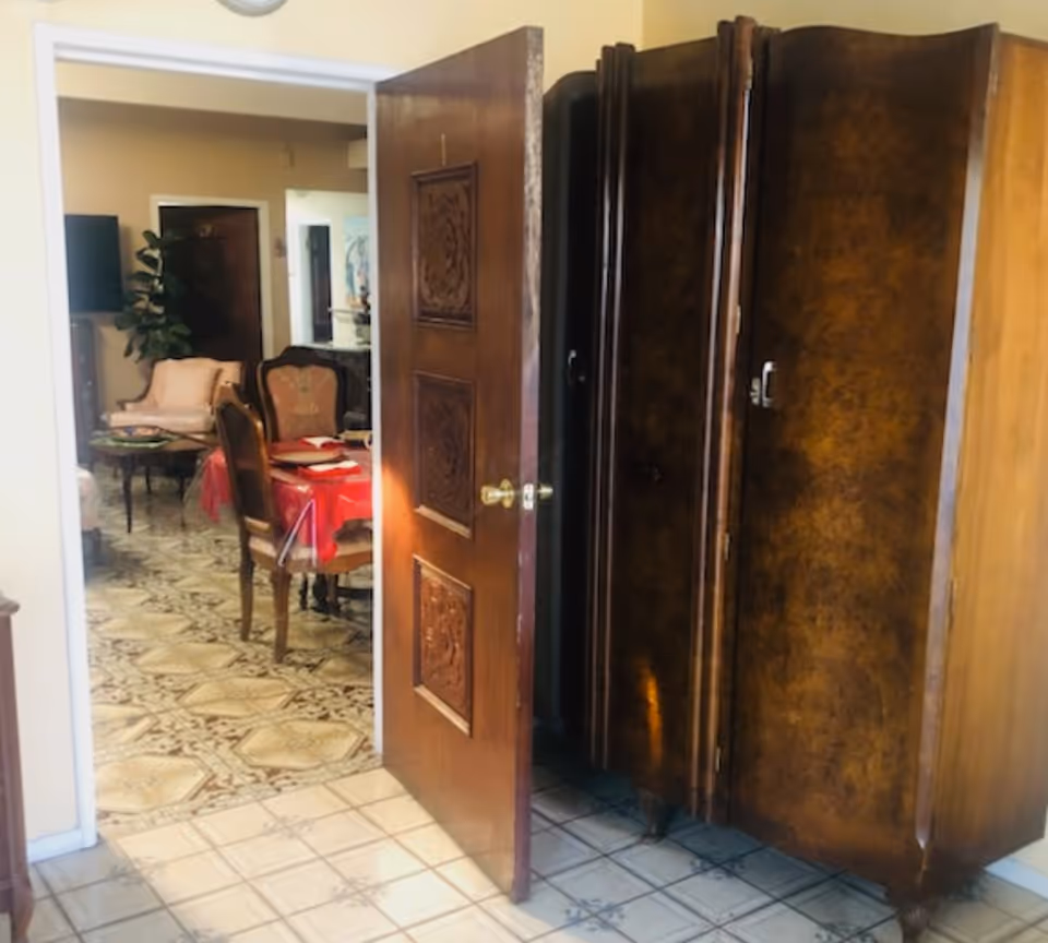 Open doorway shows a dining area with chairs and a red-tablecloth table, alongside a large armoire.