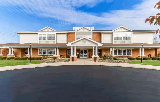 Two-story senior living facility facade with brick and light siding, central entrance, and manicured landscaping.