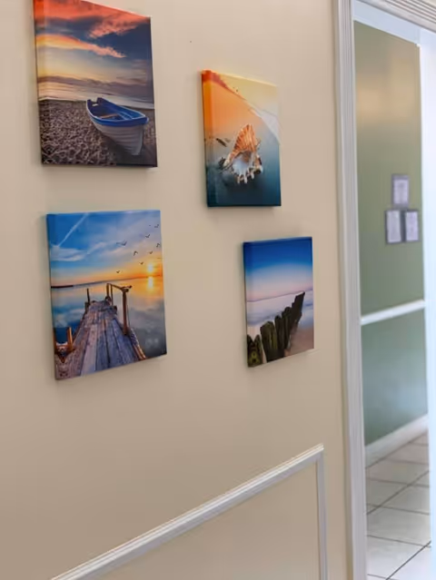 Interior hallway wall decorated with four small beach-themed canvas prints beside a doorway.