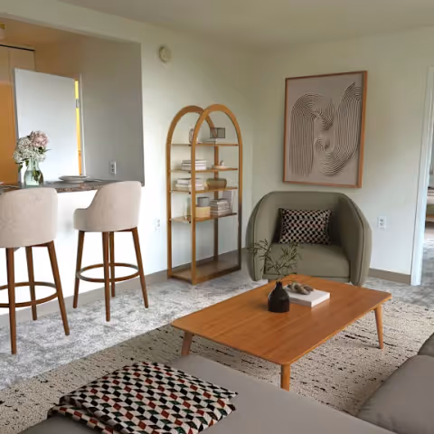 A cozy senior living lounge with a wooden coffee table, a curved armchair, a tall bookshelf, wall art, and bar-height stools at a nearby counter.