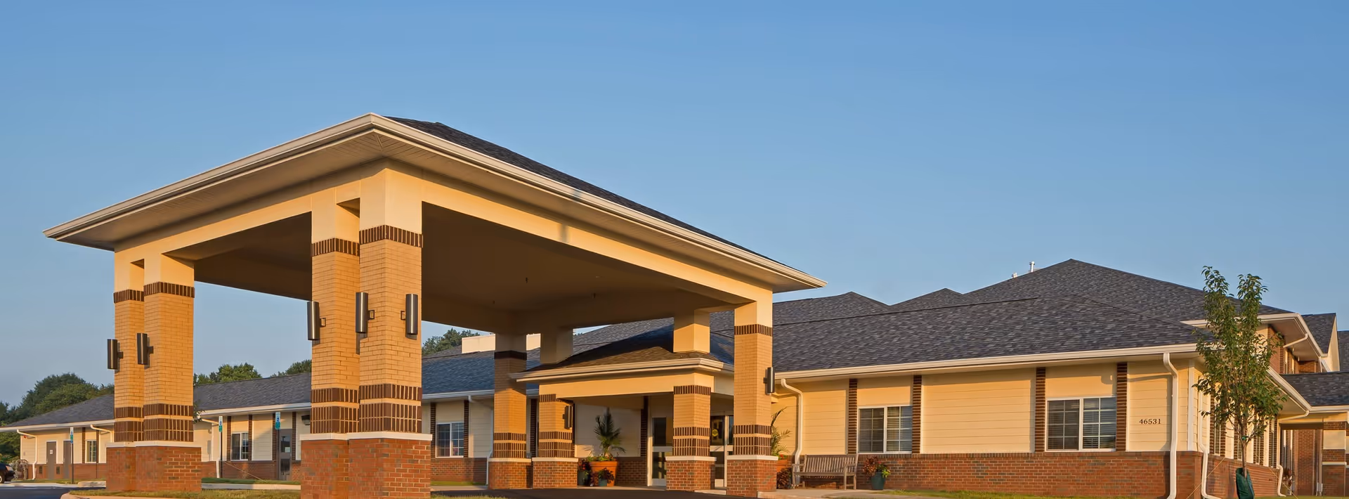 Single-story senior living facility with a large covered entrance (porte-cochere) and landscaped grounds under a clear sky.