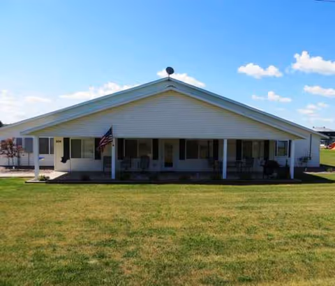 A single-story white senior living facility with a wide front porch and lawn.
