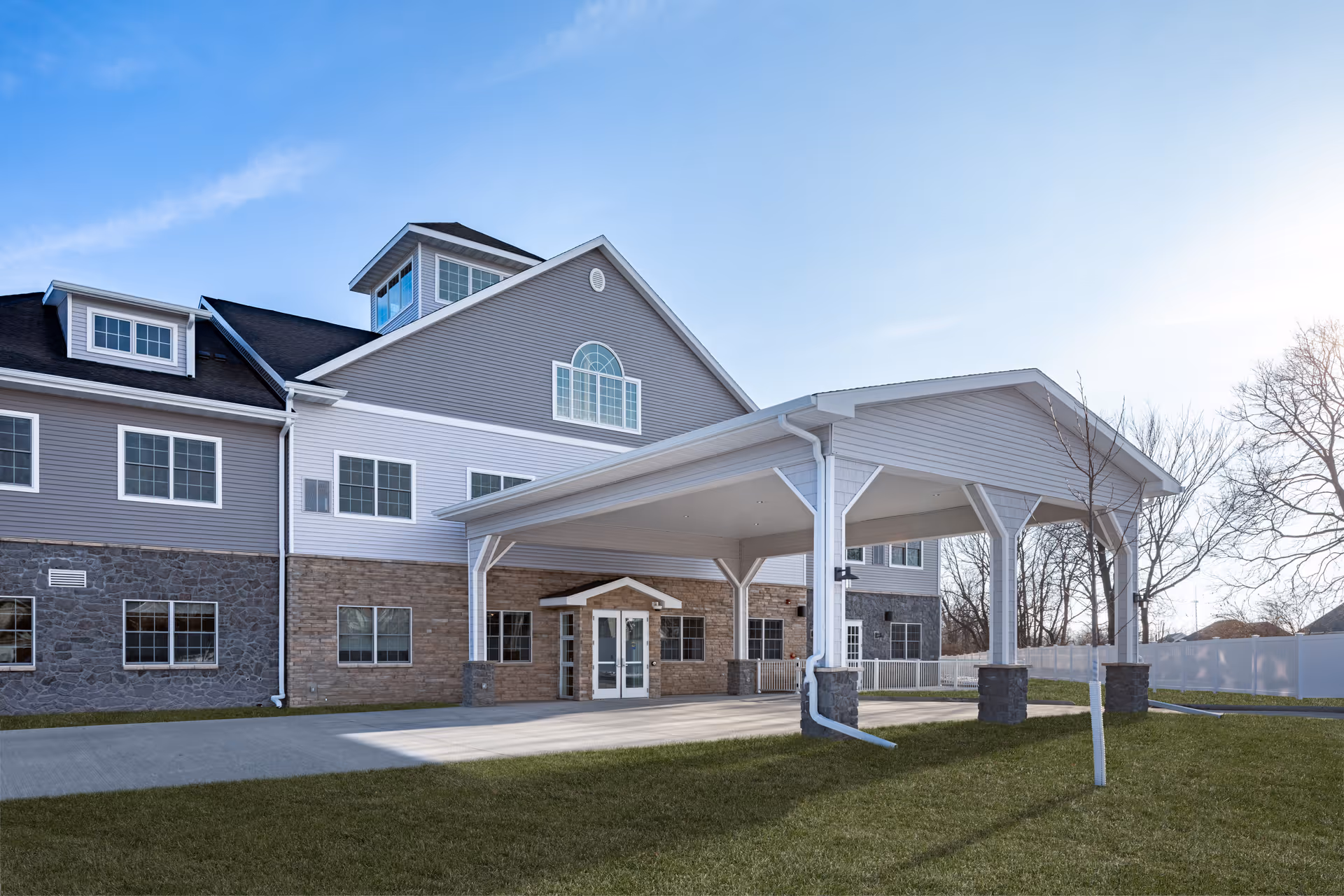 Exterior front entrance of a multi-story assisted living building featuring a large covered porte-cochere and grassy lawn.