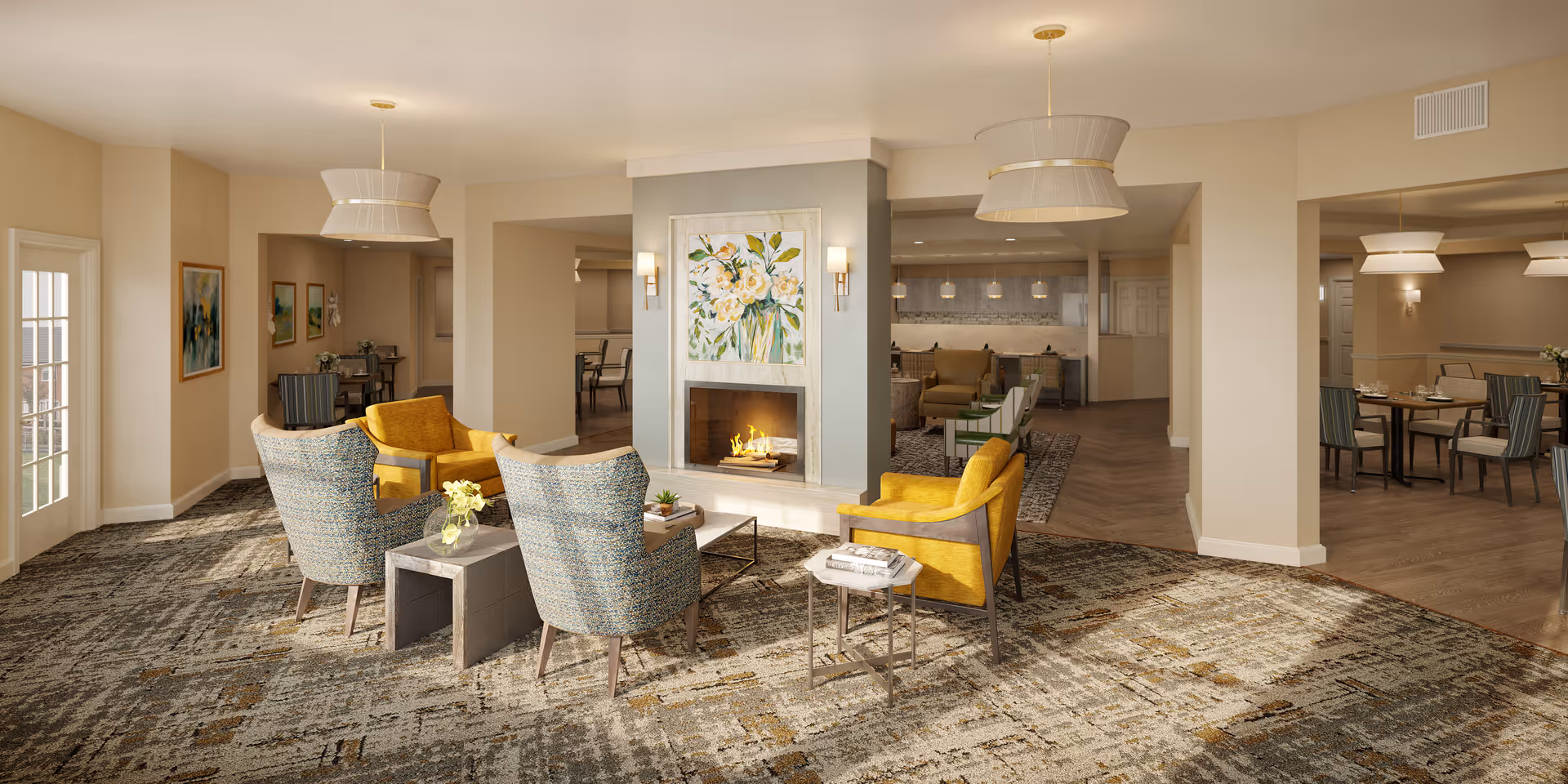 A spacious and well-lit living room area in an assisted living facility featuring a central fireplace with floral artwork above it. The room has comfortable seating including yellow and patterned armchairs arranged around small tables. The space extends into a dining area with tables and chairs, and the decor is warm and inviting with neutral tones and modern light fixtures.