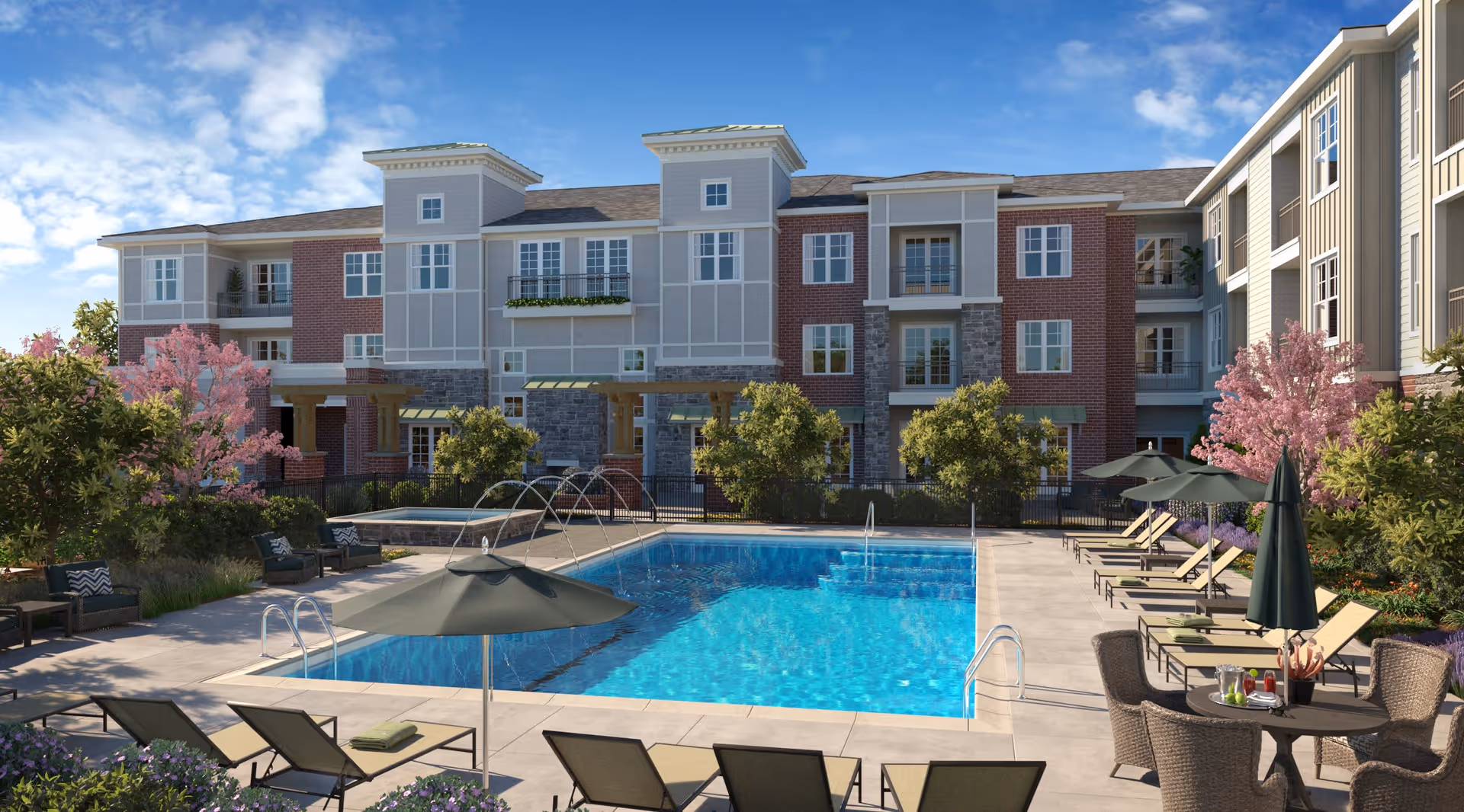 Outdoor swimming pool area at Everleigh Naperville with lounge chairs, umbrellas, tables with chairs, surrounded by trees and shrubs, and a multi-story residential building in the background under a blue sky with some clouds.
