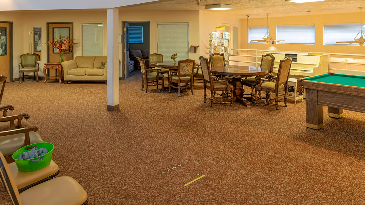 Spacious senior living common room with seating areas, dining tables, a piano and a pool table.
