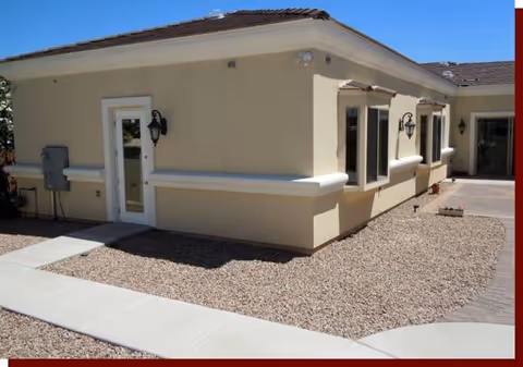 Exterior view of a beige senior living facility with gravel landscaping and a curved walkway.