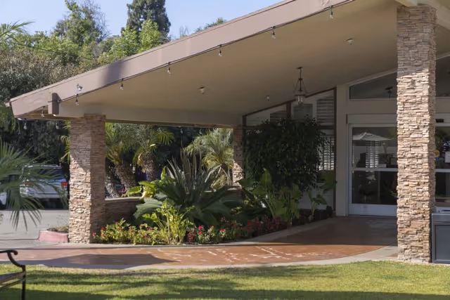 Covered front entrance with stone pillars, hanging lights, and landscaped plants at a senior living facility.