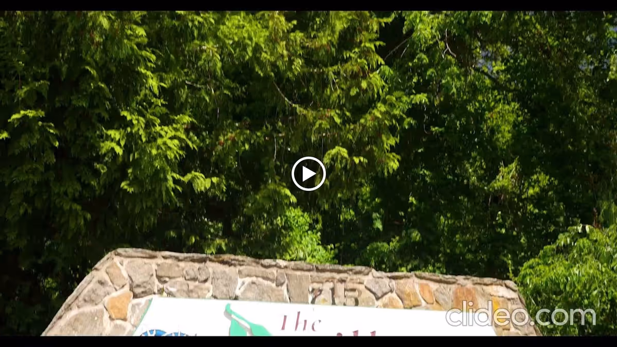 A stone entrance sign for The Village at Waterman Lake partially visible in front of dense green trees.