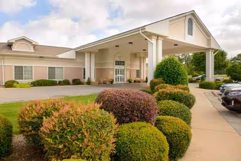 Exterior view of Life Care Center of Haltom entrance with landscaped shrubs and parked cars.