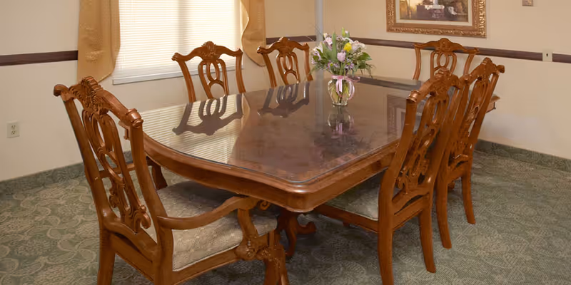 Formal wooden dining table with carved chairs and a vase of flowers in a dining room.