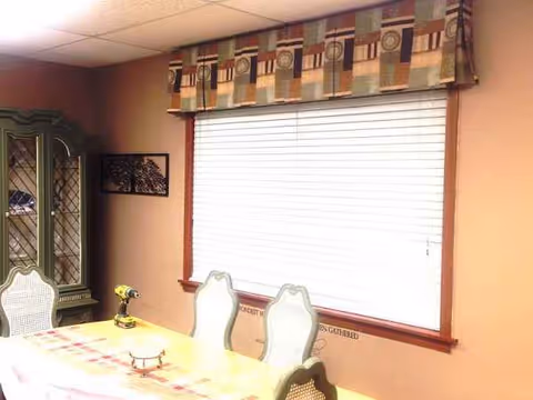 Dining room with table, chairs, window blinds, and a decorative cabinet in warm tones.