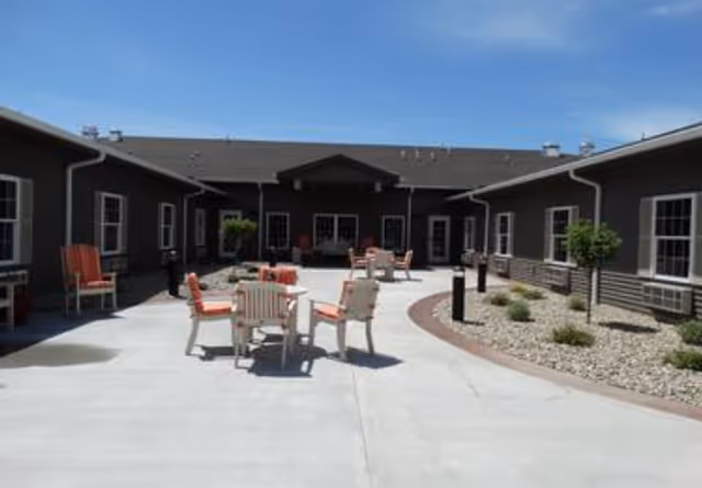 Sunny courtyard with round tables and chairs on a concrete patio surrounded by a single-story building.