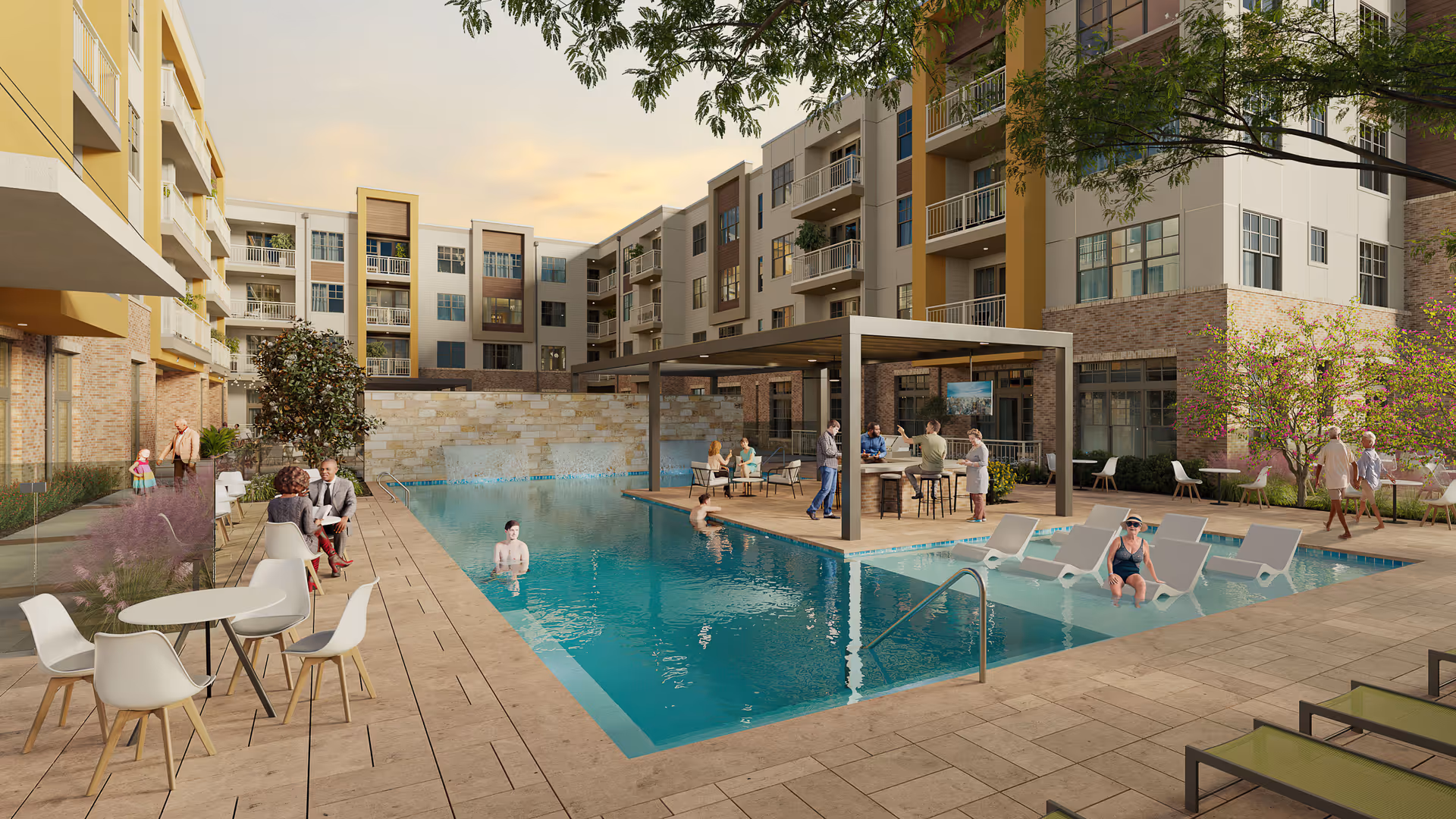 Outdoor pool area at The Jovie at Pflugerville with people relaxing and socializing around the pool. The pool has lounge chairs partially submerged in the water, a shaded seating area with tables and chairs, and a multi-story residential building in the background.