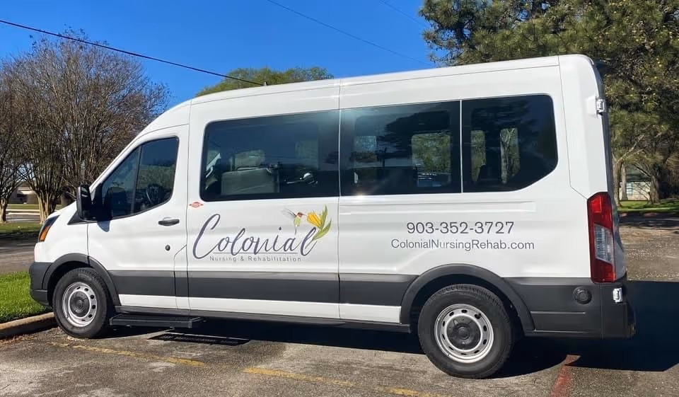 White Colonial Nursing & Rehabilitation passenger van parked outdoors with the facility logo, phone number, and website on its side.