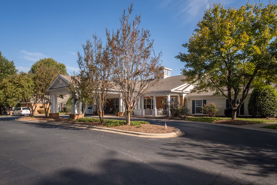 Single-story assisted living facility with a curved driveway, trees, and a wide front entrance.
