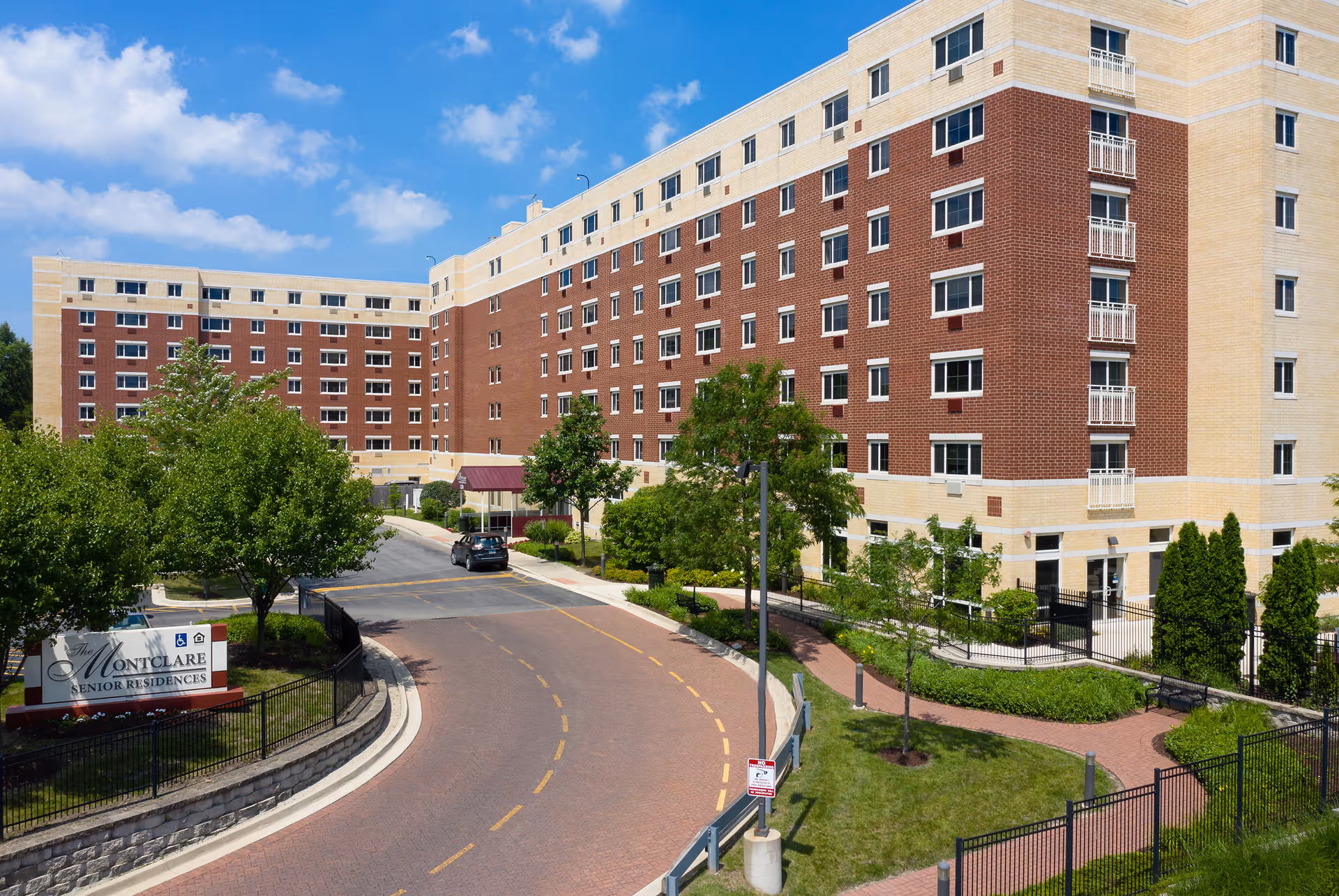 Multi-story red-brick and beige senior residence building with a curved entrance driveway, landscaping, and a sign reading 'Montclare Senior Residences'.