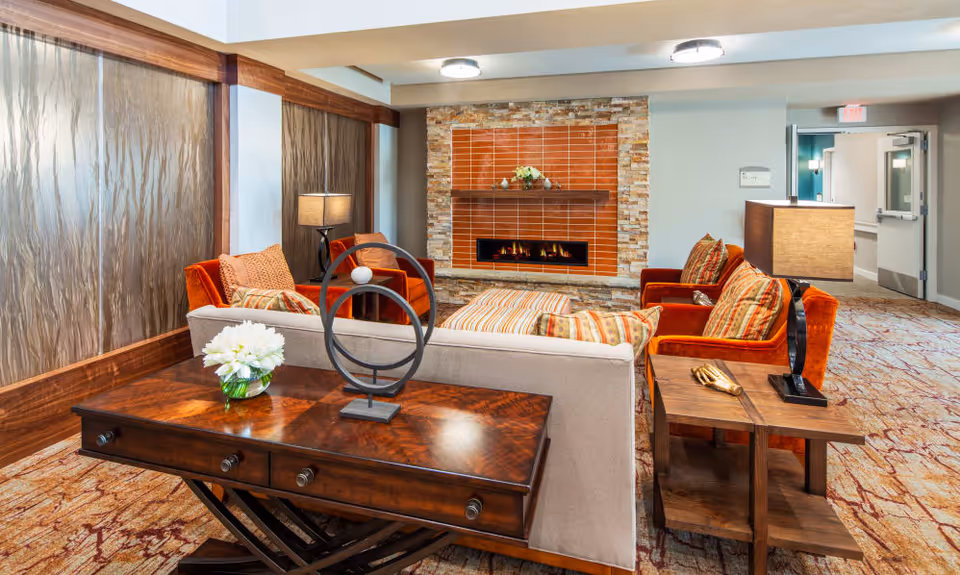 Cozy lounge area with sofas and orange armchairs arranged around a modern fireplace and a wooden console table.