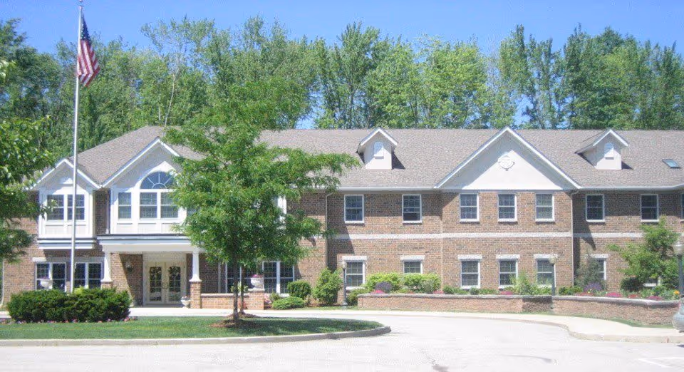Front view of Village of the Falls Assisted Living Community building with flagpole and trees.