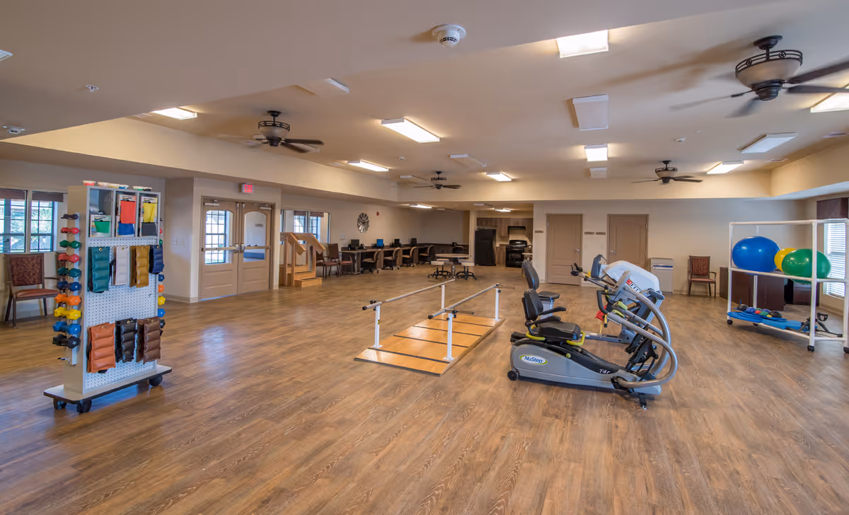 Large indoor therapy and exercise room with recumbent bikes, parallel walking bars, free weights and exercise balls.
