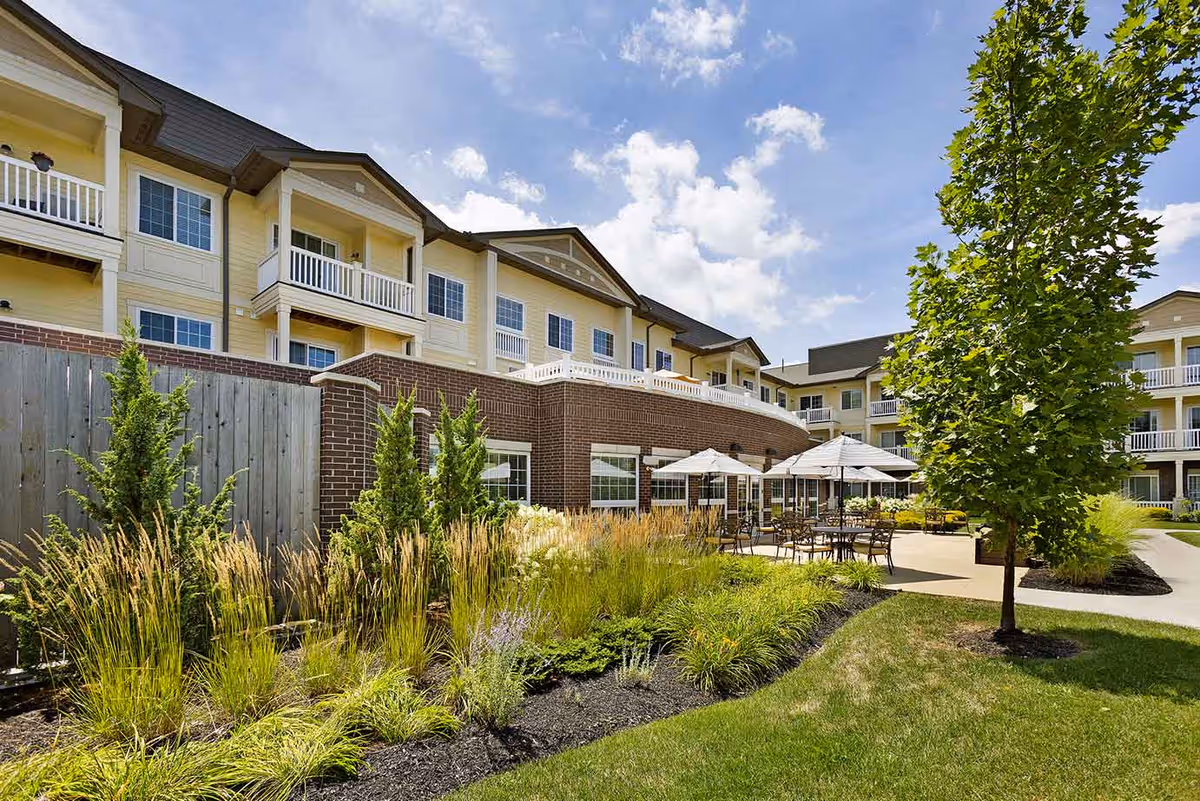 Exterior courtyard of a multi-story senior living building with balconies, patio seating and landscaped grounds.