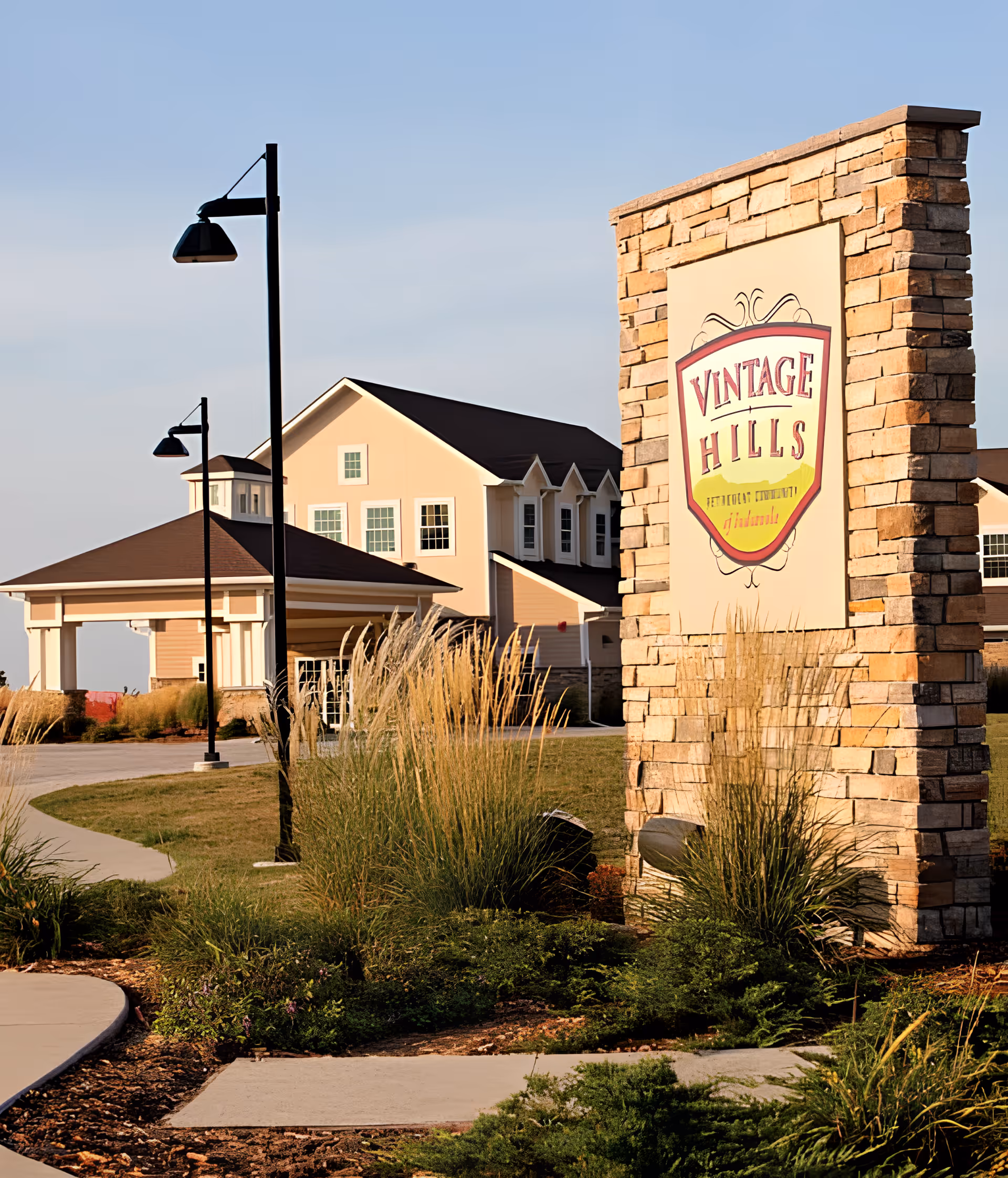 Stone entry sign reading "Vintage Hills" beside a landscaped driveway and the front of a multi-story senior living building.
