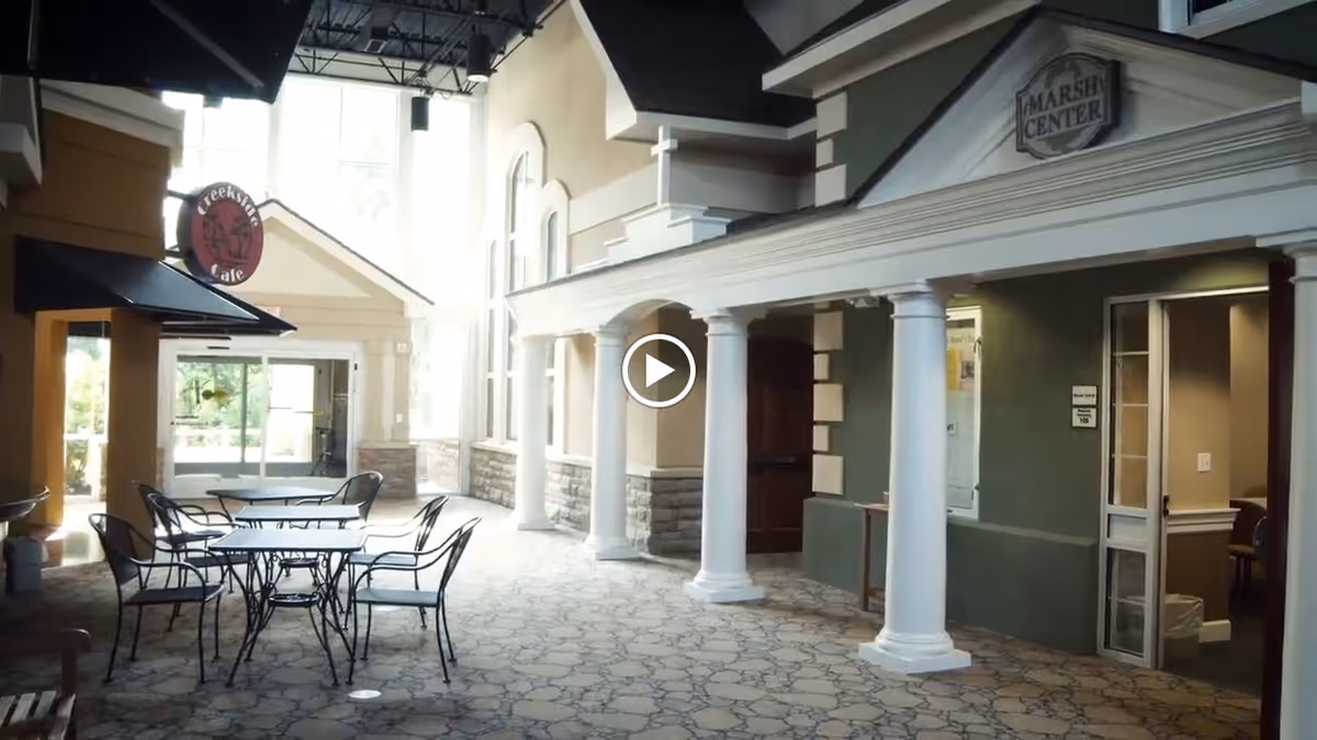 Indoor communal corridor resembling a small indoor street with café tables, storefront facades and white columns.