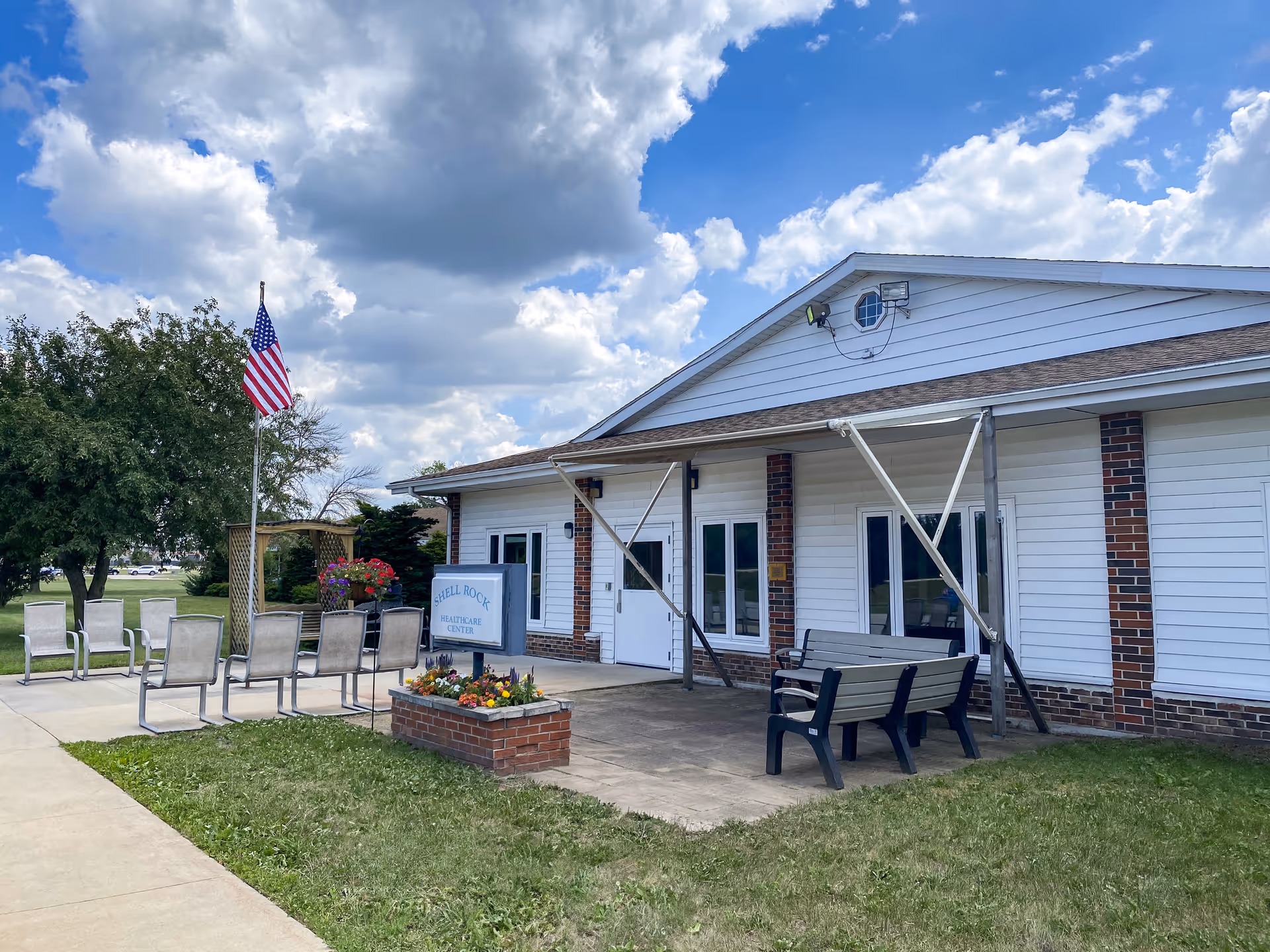 Exterior view of Shell Rock Health Care Center with seating and an American flag.