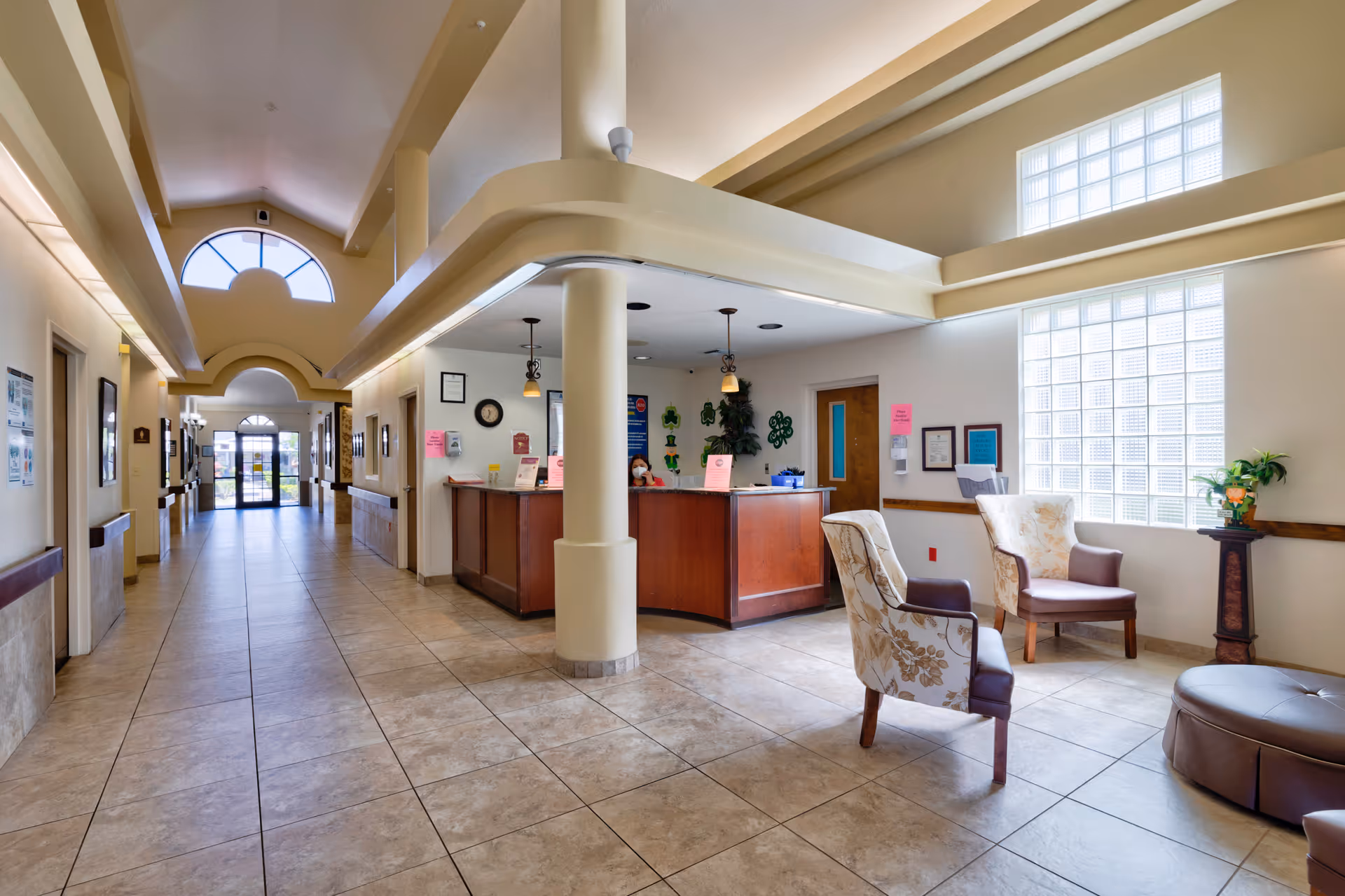 Reception lobby with a central front desk, seating area, and a long tiled corridor leading to the entrance.
