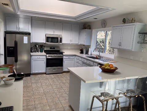 Bright modern kitchen with white cabinets, a center island with a fruit bowl, stainless steel appliances, a skylight, and tiled floor.