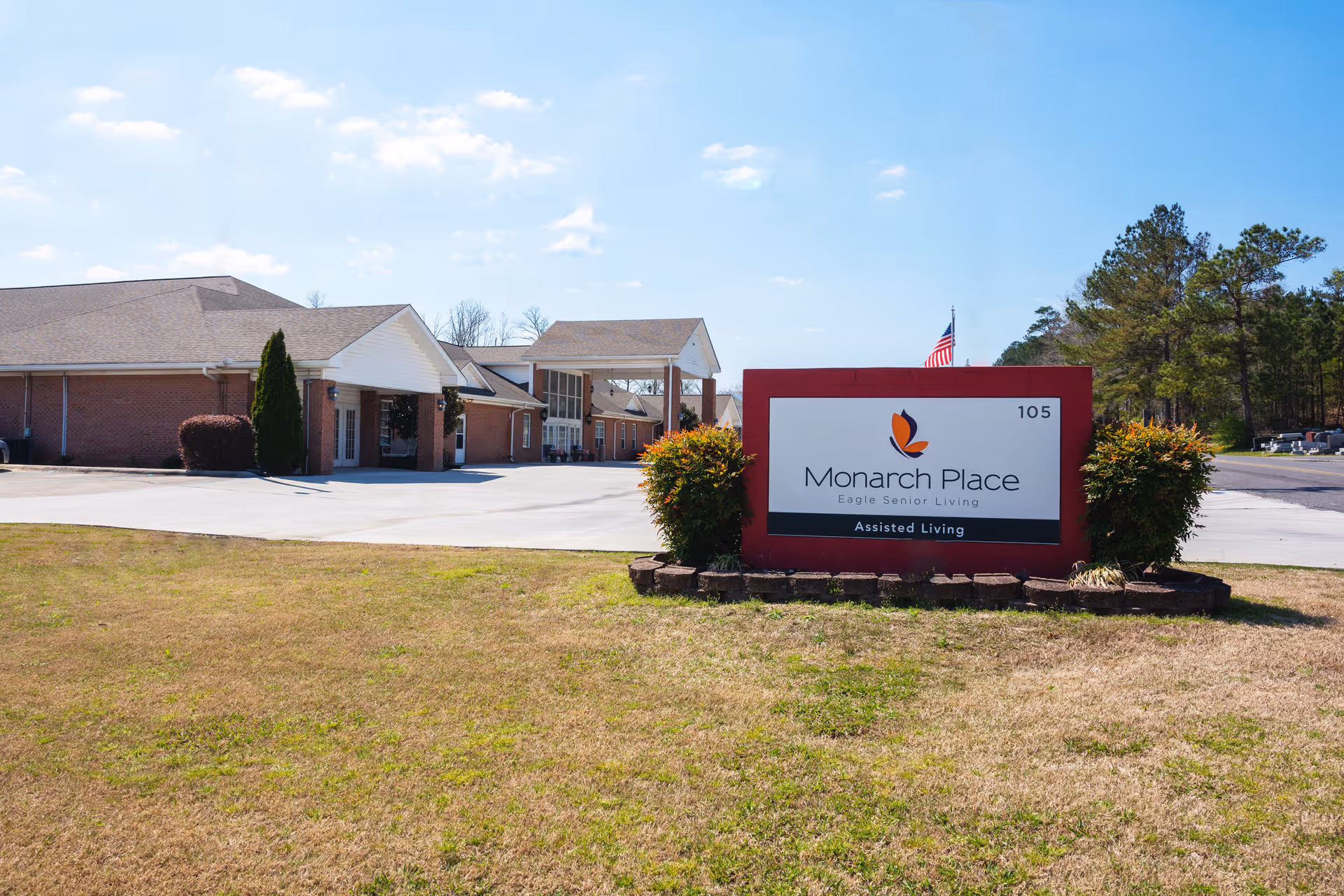 Front exterior of Monarch Place assisted living facility showing the building and a large entrance sign on the lawn.