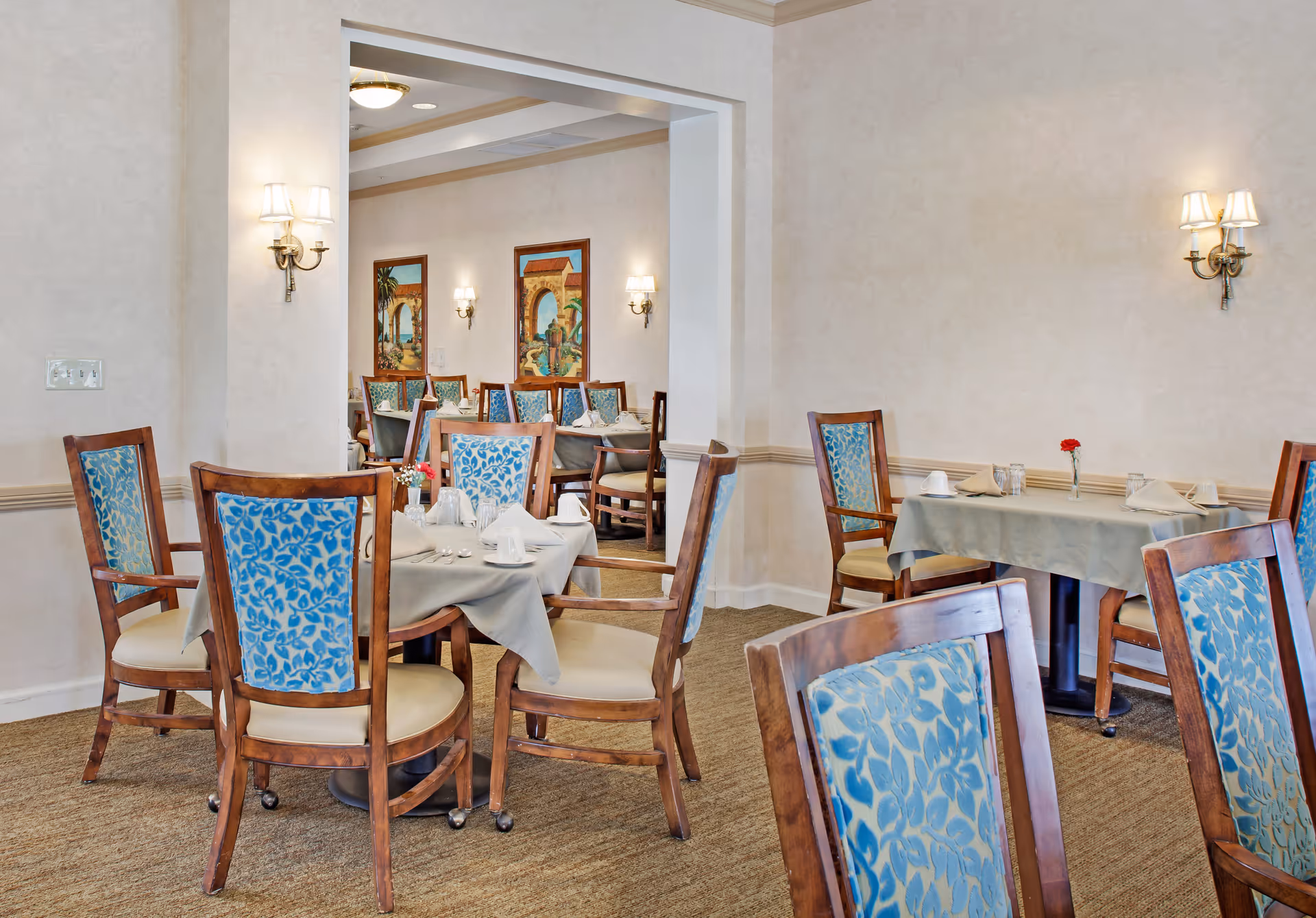 Dining room with set tables and wooden chairs featuring blue patterned upholstery.