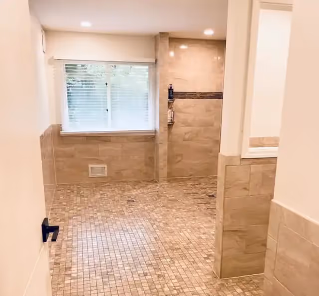 Tiled walk-in bathroom with mosaic floor, beige wall tiles, a recessed shower niche, and a window with blinds.