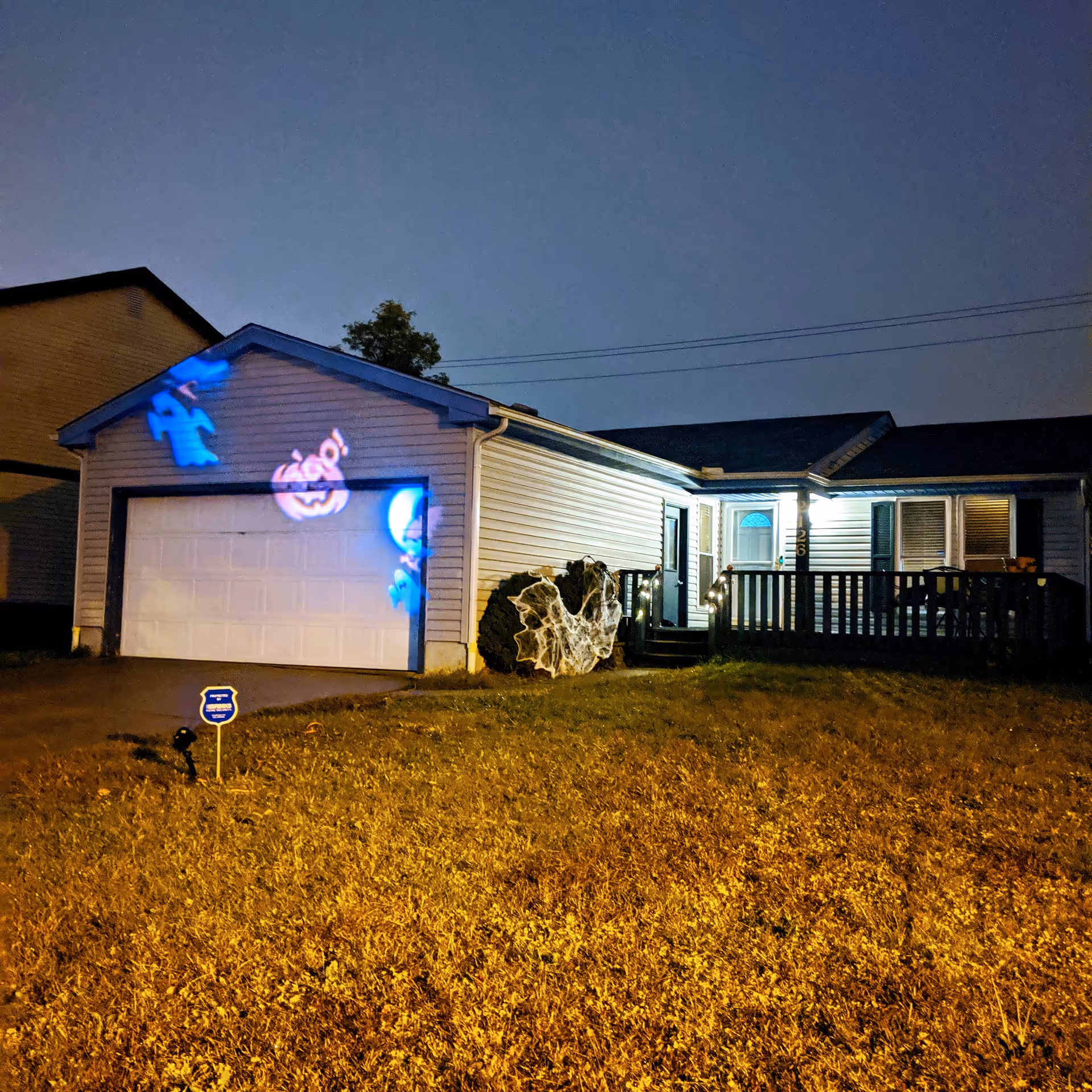 Front of a single-story house at night with a lit porch and Halloween projections on the garage door.