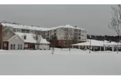 Snow-covered grounds and a multi-story senior living building with smaller outbuildings and a gazebo under an overcast sky.