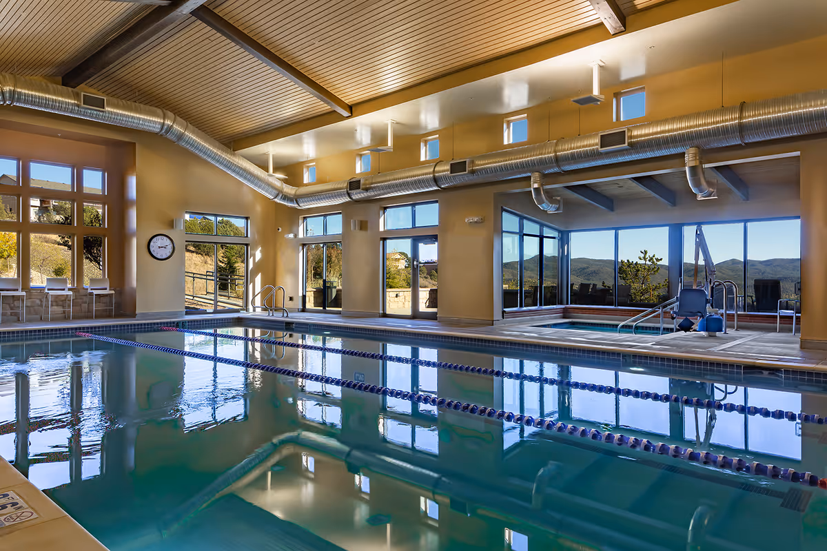 An indoor lap pool with lane dividers, seating, and large windows overlooking hills.