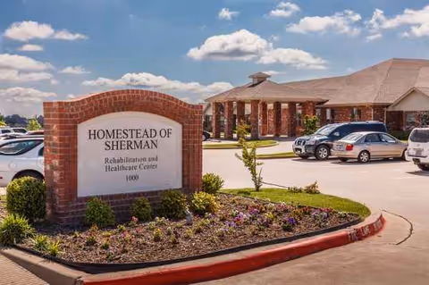 Brick sign reading Homestead of Sherman near the building entrance with a parking lot.
