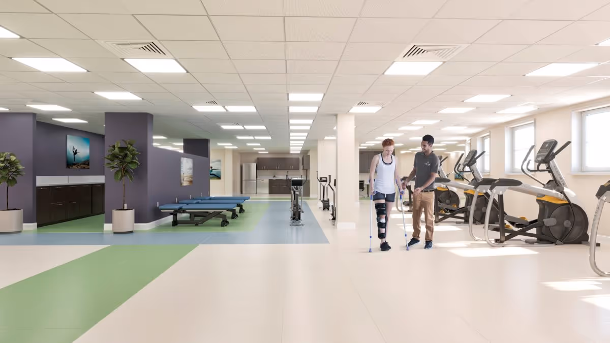Bright rehabilitation gym interior with exercise machines and a staff member assisting a person using crutches and a leg brace.